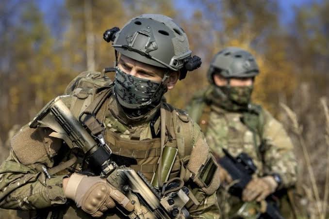 Two protective-security professionals moving through open ground in a considered, low-profile formation.
