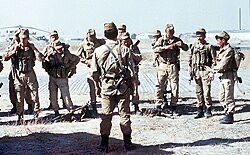 A group receiving a briefing in an open staging area before a planned movement.