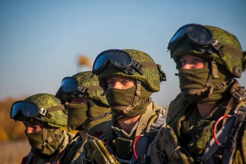 A line of uniformed personnel standing in formation against a clear sky, equipment prepared and attention forward.