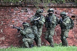 A small team assessing an approach along a perimeter wall before committing to a movement.