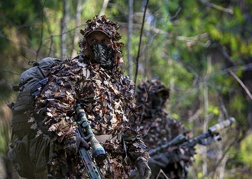 A specialist in heavy field camouflage moving through woodland, illustrating patience and concealment discipline.