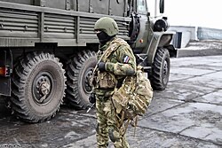 A specialist standing by a vehicle in a controlled staging area, equipment checked and accounted for before departure.